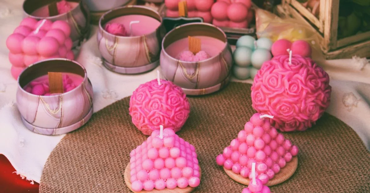 A selection of vibrant pink handmade candles in various shapes, perfect for home decor.